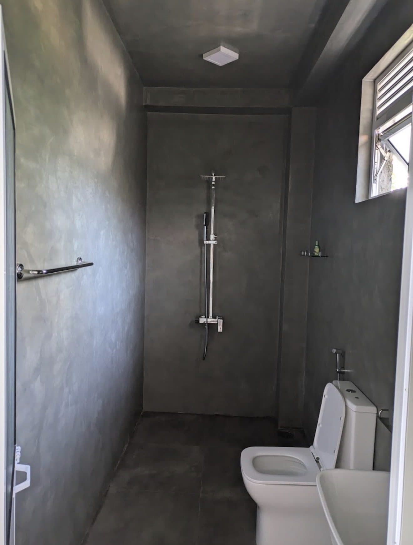 The attached bathroom with a rain shower and polished concrete walls
