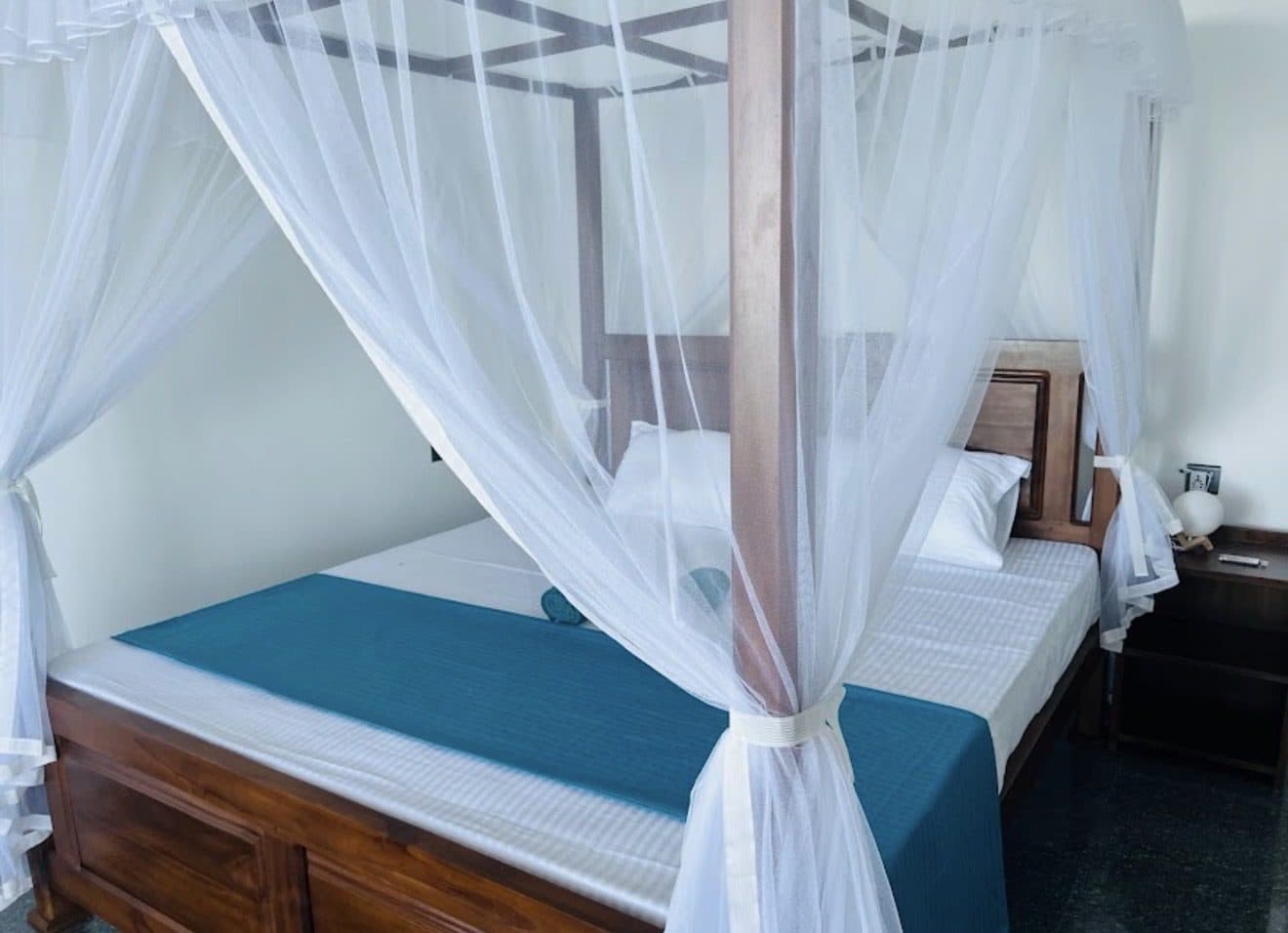 The bed close up, with its white mosquito net and teal cover