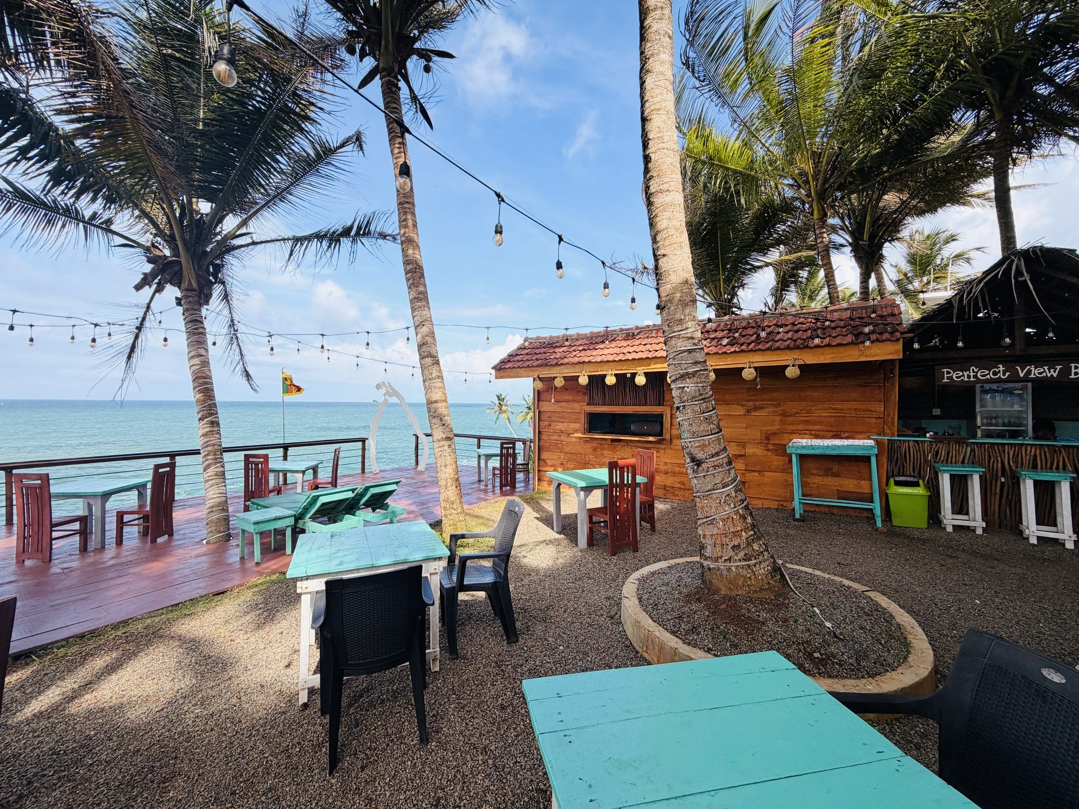 The bar and the terrace tables under the palms on a bright day, the sea behind